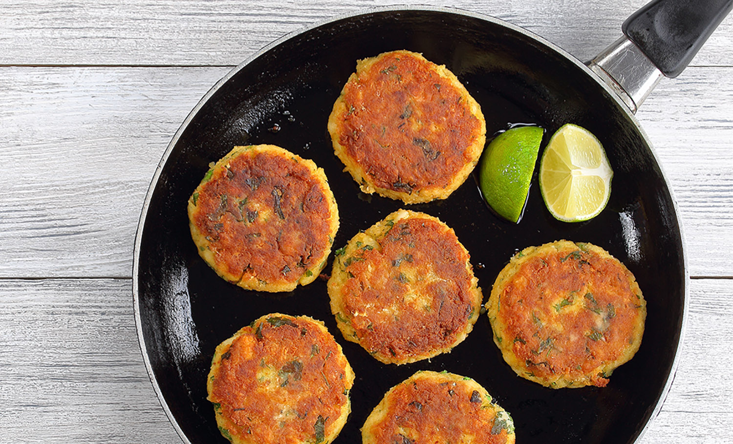 delicious fresh fried fish cakes on skillet with lime slices, authentic recipe, view from above
